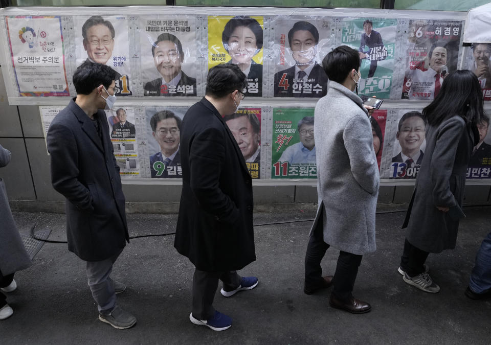 People watch posters of presidential candidates as they wait to cast their early votes for the March 9 presidential election at a local polling station in Seoul, South Korea on March 4, 2022. An unusually bitter election season in South Korea culminates on Wednesday, March 9 when tens of millions of voters pick their next president. The winner, who will be sworn into office in May and serve one five-year term, will face crucial challenges as the leader of a fast-aging nation that's grappling with economic inequalities, soaring debt and a growing North Korean nuclear threat. (AP Photo/Ahn Young-joon)