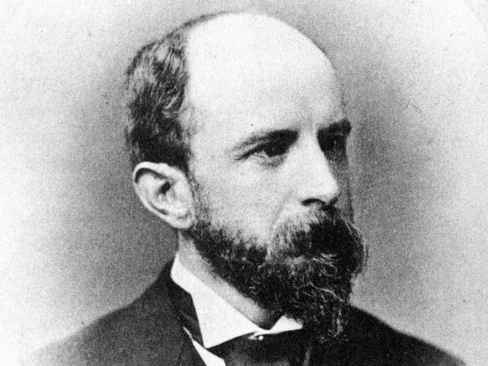 A black and white portrait of Henry Brooks Adams wearing a suit and tie while looking to his left.