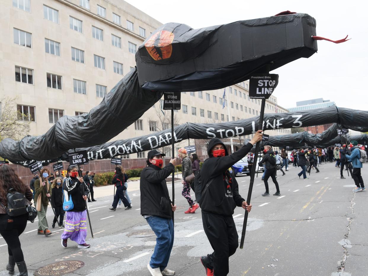 Native youth protesters carry a long cardboard black pipe with a snake head which reads "Shut down DAPL" and "Stop line 3" down the street in Washington DC