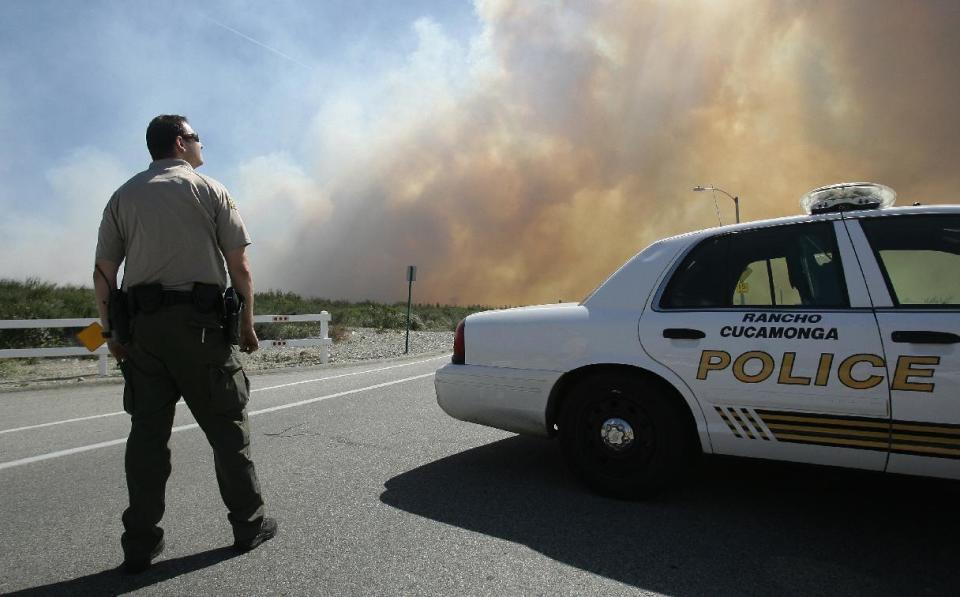 A San Bernardino Sheriff's deputy keeps an eye on a brush fire burning in Day Creek near the Etiwanda Perserve in Rancho Cucamonga, Calif., on Wednesday, April 30, 2014. Fire officials say winds gusting to 60 mph are pushing the flames through the foothills of the San Bernardino Mountains east of Los Angeles, although no homes are in immediate danger. Several neighborhoods and at least seven schools in Rancho Cucamonga have been evacuated. There’s no word on what sparked the blaze but it comes in the midst of a heat wave that’s created extreme fire danger. (AP Photo/The Press-Enterprise, Stan Lim) MAGS OUT; MANDATORY CREDIT