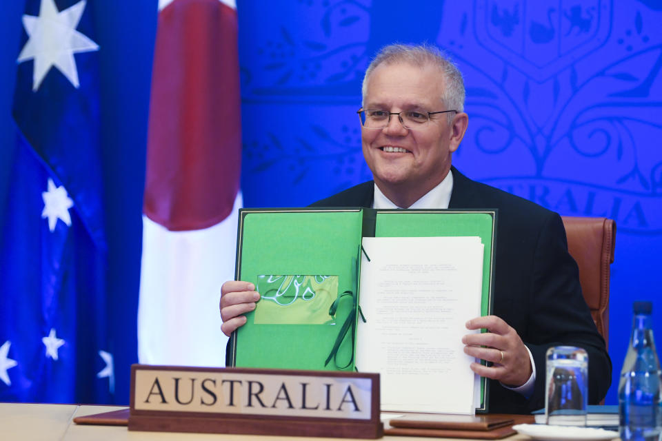Australian Prime Minister Scott Morrison holds up a signed document during a virtual treaty signing summit with Japanese Prime Minister Fumio Kishida, at Parliament House, in Canberra, Australia, Thursday, Jan. 6, 2022. The leaders of Japan and Australia signed a “landmark” defense agreement Thursday that allows closer cooperation between their militaries and stands as a rebuke to China's growing assertiveness in the Indo-Pacific region. (Lukas Coch/AAP Image via AP)