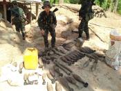 In this photo provided by Karen National Liberation Army, a Karen National Liberation Army soldier holds a motor shell while standing next to a cache of mortar shells found at a Myanmar military outpost Friday, May 7, 2021, in Mutraw district, Karen State, Myanmar. Ethnic Karen guerrillas burned down a Myanmar military outpost Friday morning, capturing it without a fight after its garrison fled at their approach, a senior Karen officer said. (Karen National Liberation Army via AP)