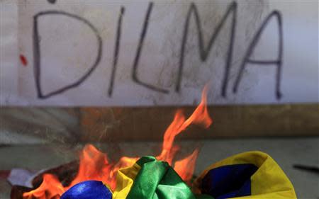 A Brazilian flag burns in front a wall graffiti referring to Brazilian President Dilma Rousseff during a protest on Brazil's Independence Day in Rio de Janeiro September 7, 2013. REUTERS/Ricardo Moraes