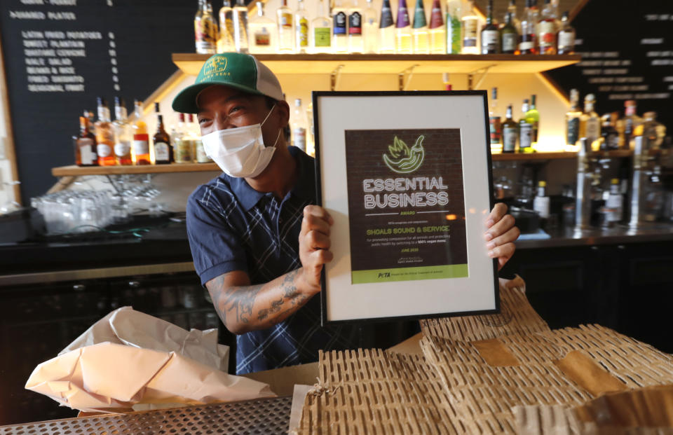 Omar Yeefoon, owner of Shoals Sound & Service vegan restaurant, laughs and shows an award from PETA he had just unwrapped, Tuesday, June 30, 2020, in Dallas. Yeefoon reopened his Dallas restaurant June 10 to "a pretty good reception," after having been shuttered for three months. The comeback was fleeting. After four days, Yeefoon had to shut down again in the face of a COVID-19 resurgence in Texas and lay off two of the four workers he'd brought back. (AP Photo/LM Otero)