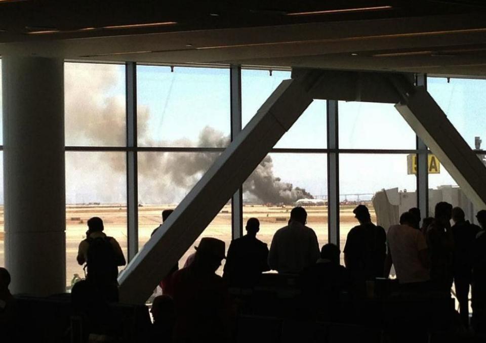 People at the airport look out at the burning plane (<a href="https://twitter.com/Twitsnoop/status/353591155369312256" target="_blank">photo</a> via Twitsnoop)