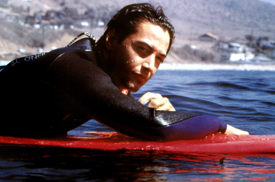 A man on a surfboard looks at the camera