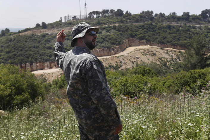 FILE - In this April 20, 2017 file photo, a Hezbollah officer, who identified himself as Ehab, stands in front an Israeli army position, background, as he explains to journalists about the defensive measures established by the Israeli forces, how they cut through the mountain to prevent against any Hezbollah infiltration into Israel, at the Lebanese-Israeli border near the village of Labbouneh, south Lebanon. Lebanon's Hezbollah militia looms large over the current Israel-Hamas war, even though it has stayed out of the fighting so far. (AP Photo/Hussein Malla, File)