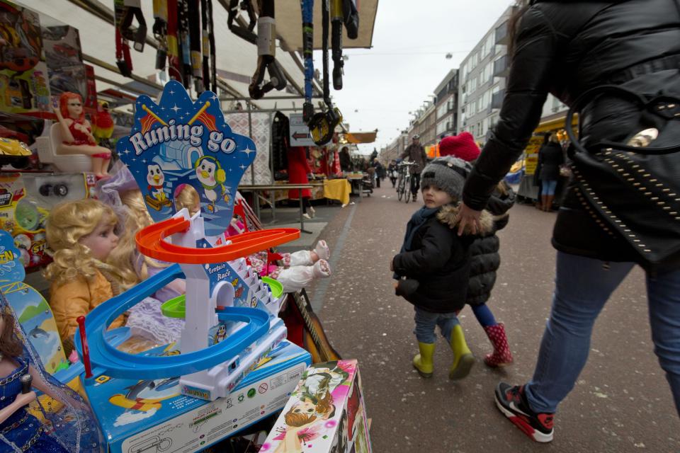 This March 20, 2013 photo shows a mother urging her children away from toys in a stand at Albert Cuyp market, Amsterdam, Netherlands. Amsterdam's wealth began in its port with the merchants who bought and sold everything from tulip bulbs to spices from the East Indies. A little of that mercantile past can still be seen at the city's many markets. The most famous is the Albert Cuyp food market in the Pijp neighborhood, which sells, as the city website puts it, everything from cheese to bicycle chains, six days a week. (AP Photo/Peter Dejong)