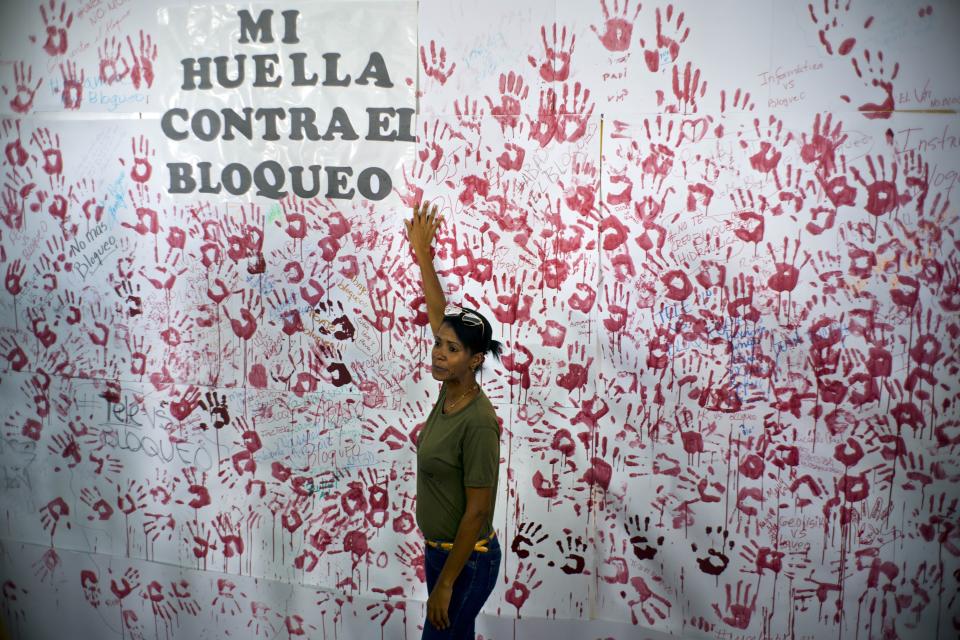 A woman poses in front of hand prints on a wall during an event against U.S. trade embargo against Cuba in Havana, Cuba, Wednesday, Oct. 31, 2018. The United Nations will vote Thursday Nov. 1 on a resolution regarding the ongoing U.S. trade embargo against Cuba. (AP Photo/Ramon Espinosa)