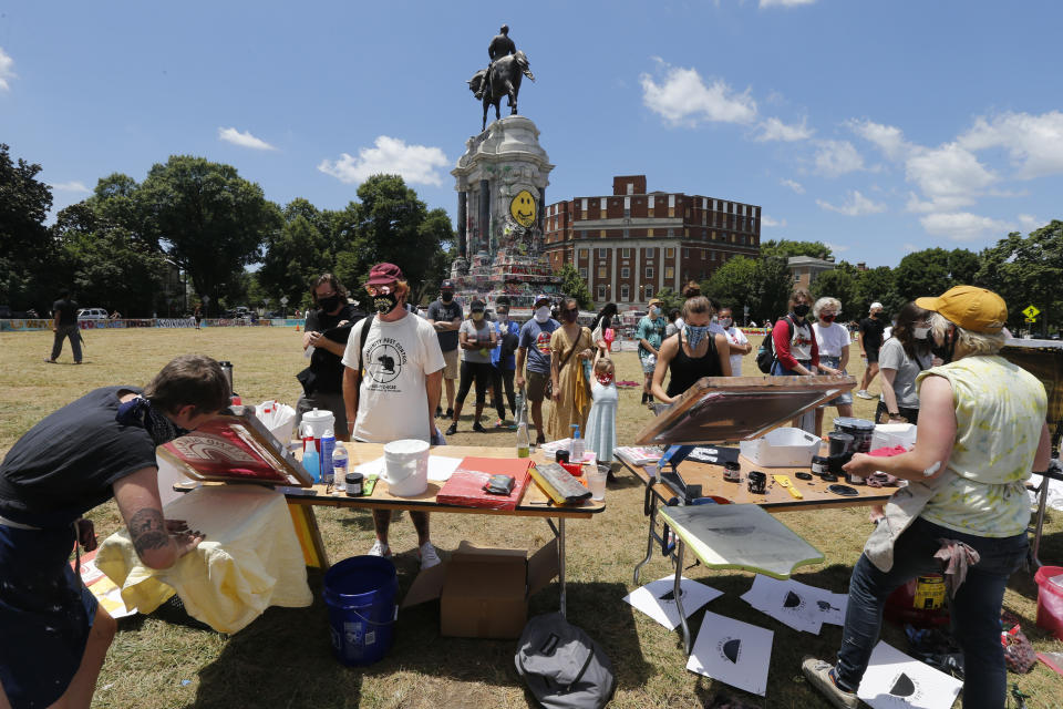 Kate Fowler, left, and KB Brown, right, who work for Studio Two Three of Richmond, work of screenprints at the statue of Confederate General Robert E. Lee on Monument Avenue Wednesday June 24, 2020, in Richmond, Va. A new vibe has emerged alongside the raucous atmosphere of protests, one that is more reminiscent of the hippie love and peace festivals of the 1960s. Each day, hundreds of people of all ages and races visit the statue, located on a busy traffic circle and surrounded by grass. The statue has become a focal point of protests for the Black Lives Matter movement in the Richmond area. (AP Photo/Steve Helber)