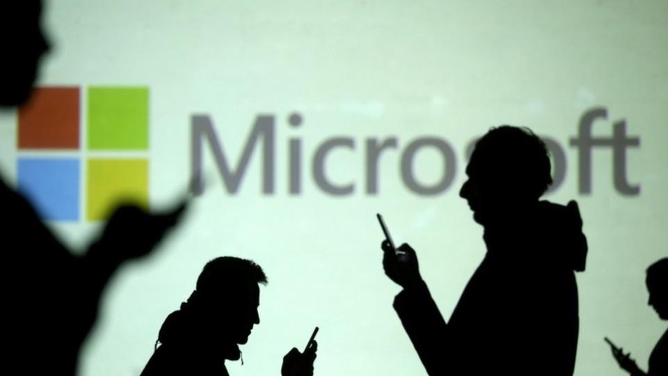 Personas manejan sus teléfonos junto a un panel de Microsoft.