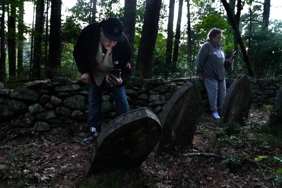 Kris Smith uses his phone light to get a better look at one of the gravestone while partner Christina Cusolito views others at a beginner-level ghost-hunting expedition at Burrillville's Conjuring house on Aug 25, 2022.