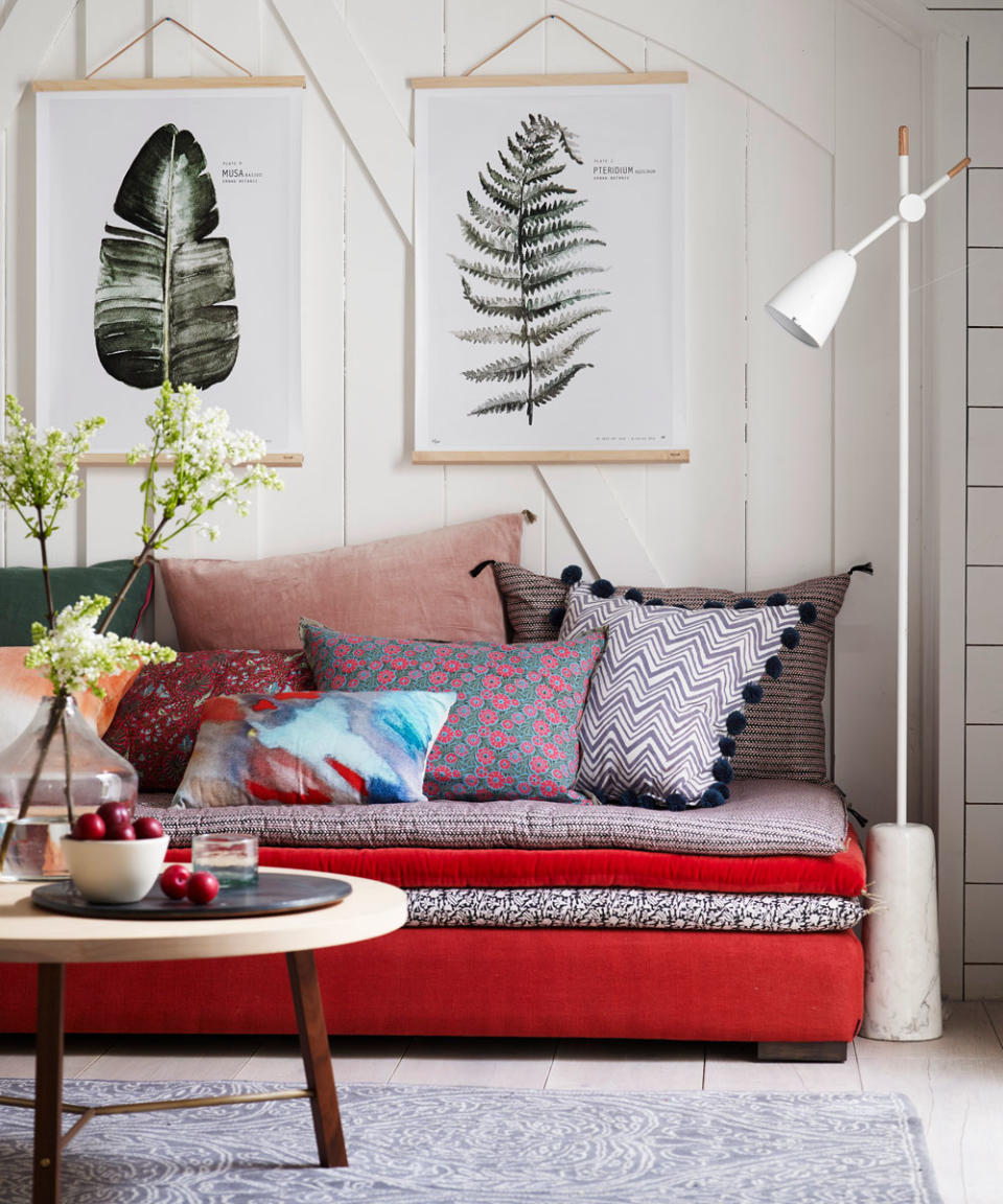 Small bedroom with sofa bed, floor lamp, round table and feather paintings on the wall