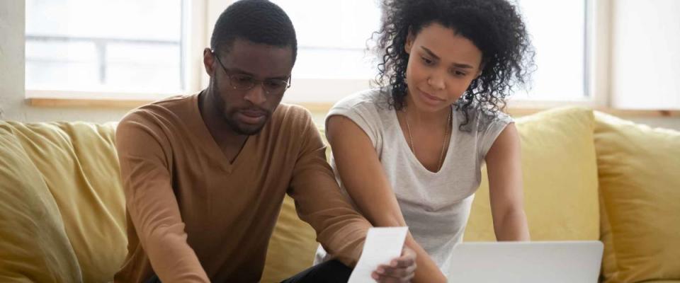 Serious african american couple using calculator and laptop for calaulating finance. Diverse upset man and woman taxing, accounting with check credit analytic for mortgage payment.