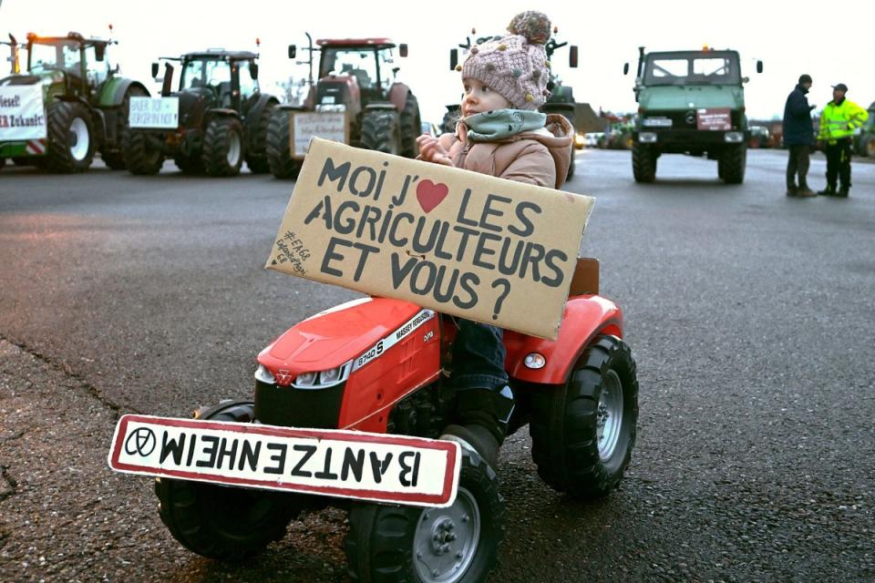 The daughter of a farmer rides on a child's tractor with a placard that reads 