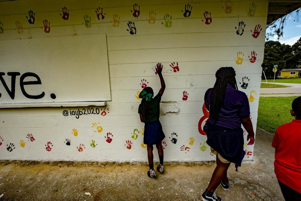 Aubrey Amos, left, adds a handprint to a mural wall at Spence Park as her cousin,  Jaleah Amos, looks on Tuesday afternoon. They are part of a nonprofit organization, Inspired Ambitious Young Believers, Inc., that created the mural to encourage young people in Mulberry to believe in themselves.