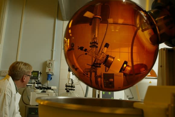 Laboratory with person in white lab coat looking at an amber-colored sphere with other equipment nearby.