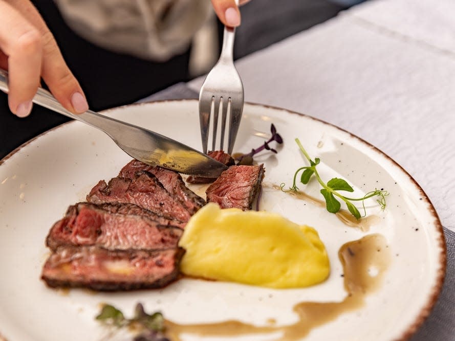 A person cutting grilled sliced steak with mashed potatoes