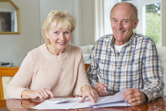 An older couple looking at paperwork, smiling as they sit side by side at a table.