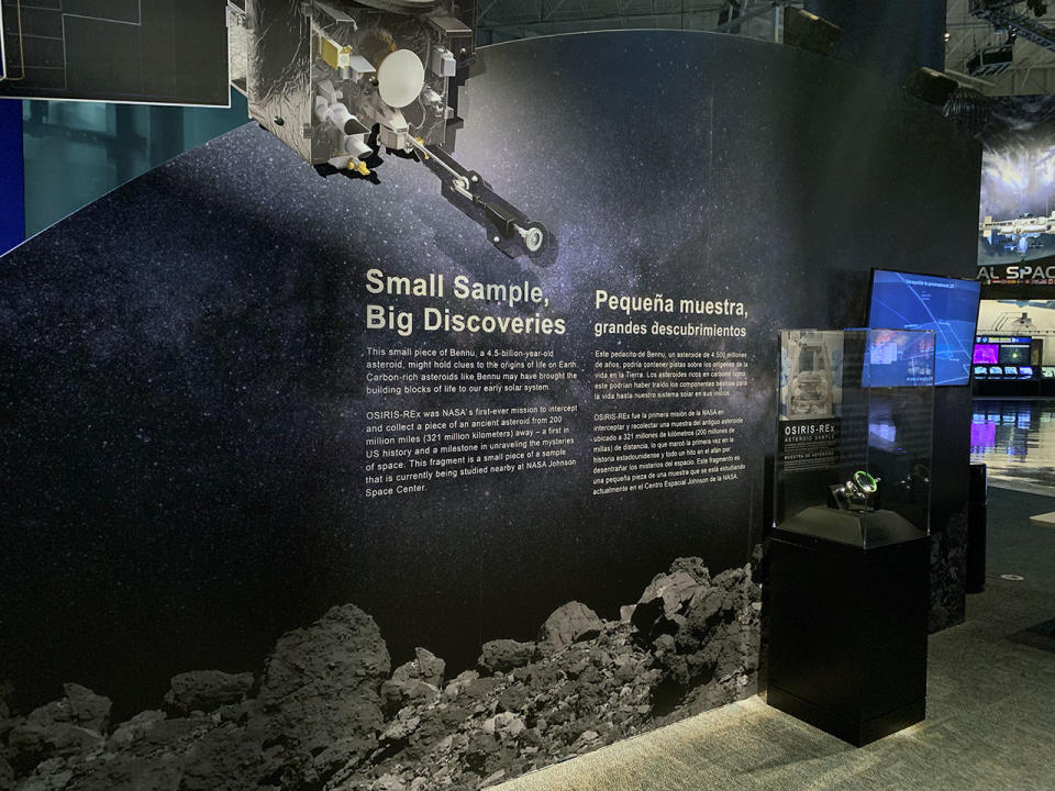 photograph of an asteroid exhibit at a space museum, showing a glass display case with a dark wall with text on it.