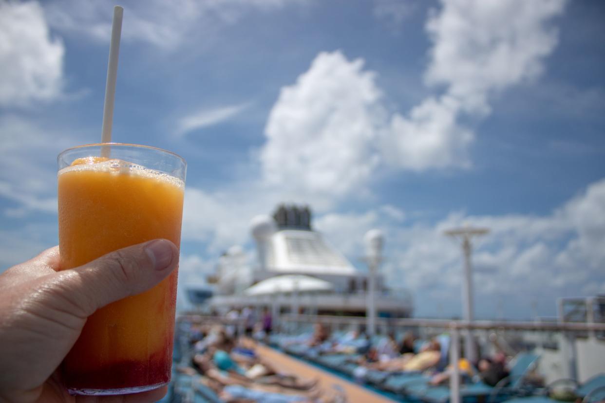 Orange and Mango Cocktail on on a cruise liner being held by a Caucasian mans left hand on beautiful tropical beach.