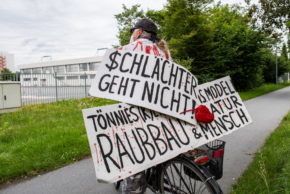 04 July 2020, North Rhine-Westphalia, Rheda-Wiedenbrück: An activist from the "Alliance Together Against the Animal Industry" stands with his bicycle and two banners with the inscription: "$chlachter geht nicht" and Tönnies (k)ein Geschäftsmodell - Raubbau an Natur & Mensch" in front of the Tönnies company complex. Photo: Guido Kirchner/dpa (Photo by Guido Kirchner/picture alliance via Getty Images)