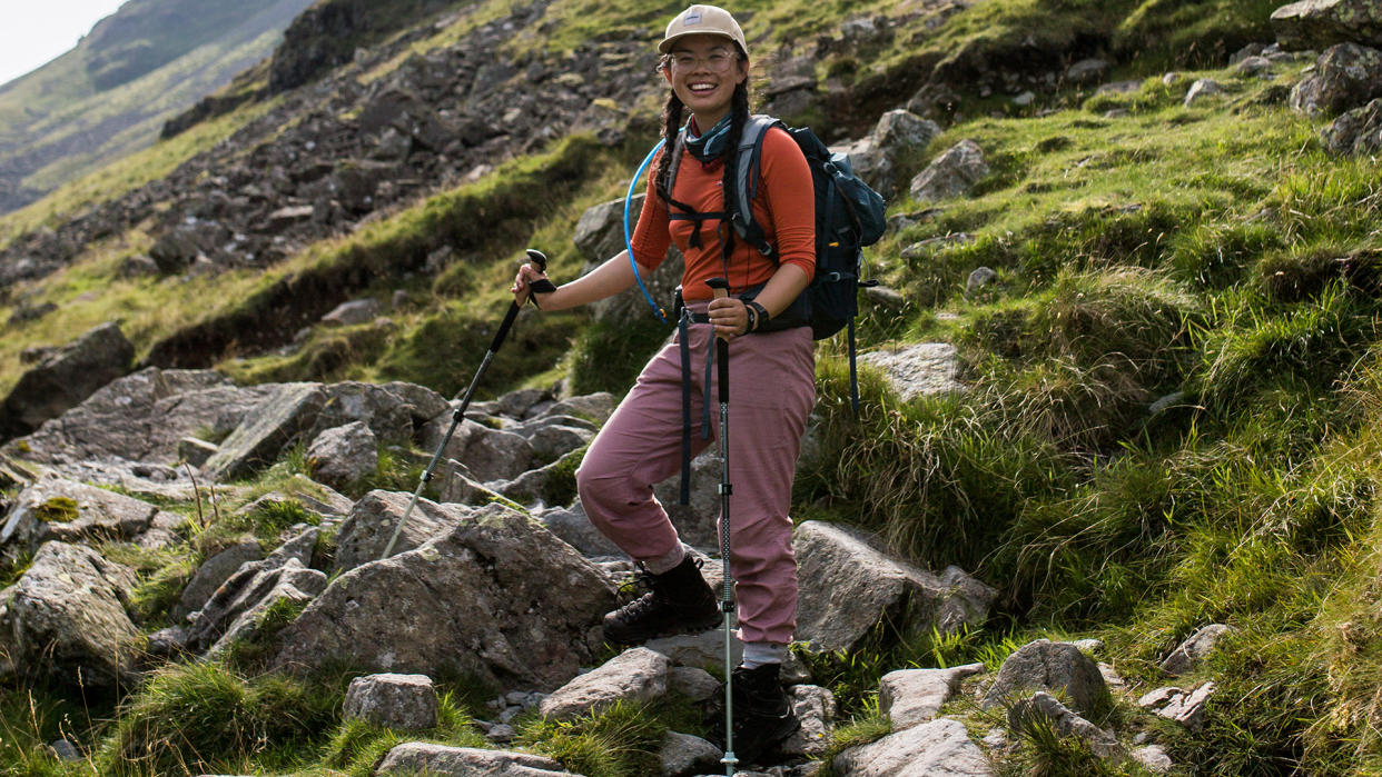  A woman stands on a rocky mountainside, holding a pair of Black Diamond Pursuit Trekking Poles. 