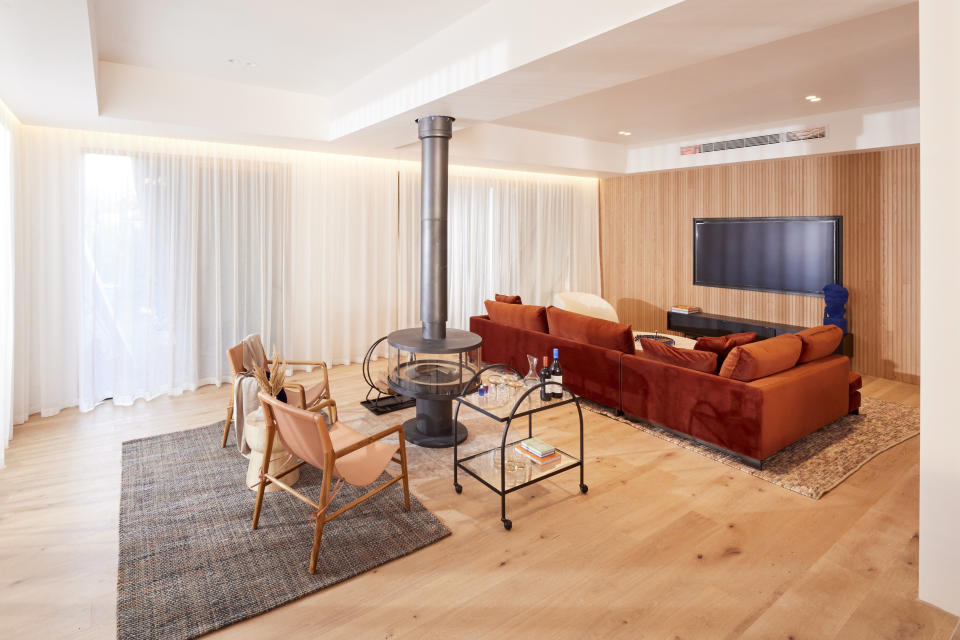 A wide shot of a living room, with a fireplace in the middle, a large sofa and tv against the far wall. 