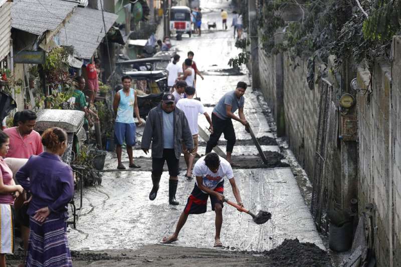 菲律賓塔爾火山12日噴發，附近民眾13日忙著清理火山灰。（美聯社）