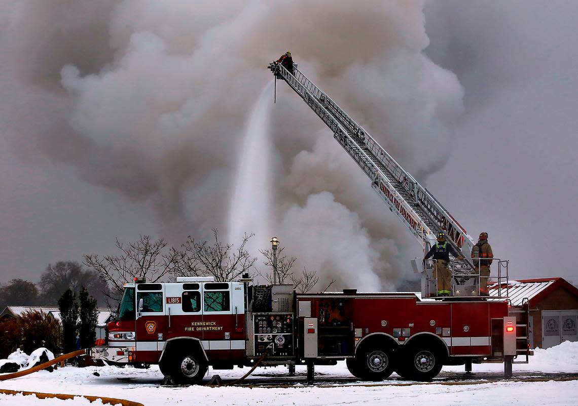 Frefighters use the Kennewick Fire Department aerial fire truck parked on land to help stop the spread of a boat house fire early Wednesday morning at the Clover Island Yacht Club in downtown Kennewick.