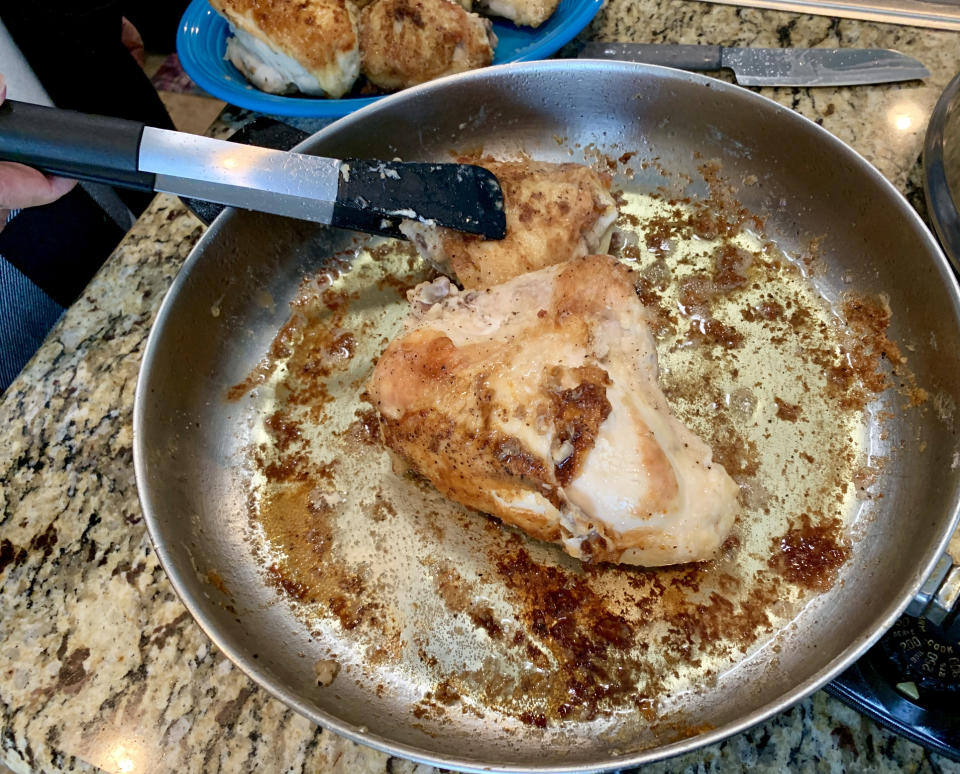 Two chicken breasts being cooked in a frying pan. One piece is being handled with tongs