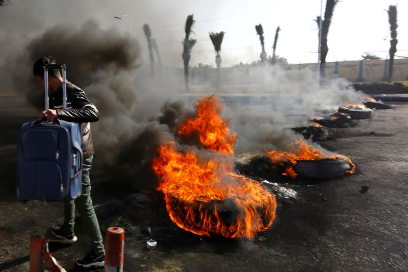 A passenger carries his bag as he walks past burning tires ignited by Iraqi protesters to block the road to the Najaf International Airport, during ongoing anti-government protests in Najaf