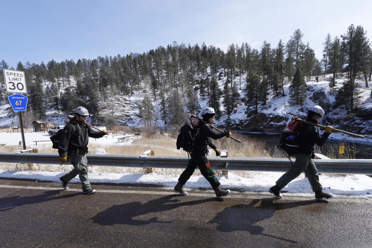 U.S. Forest Service firefighters and members of the Mile High Youth Corps head off to set fire to piles of tree debris near the Bridge Crossing picnic grounds in Hatch Gulch Wednesday, Feb. 23, 2022, near Deckers, Colo. In Colorado, climate change means snow is not always on the ground when needed so that crews can safely burn off debris piles and vegetation to help keep future wildfires from becoming catastrophic. (AP Photo/David Zalubowski)