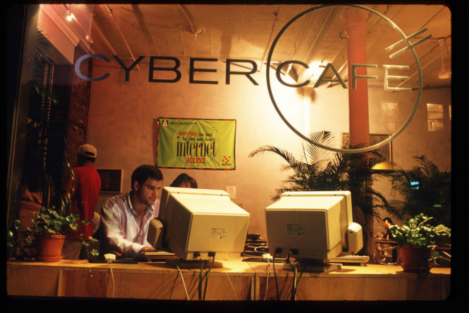 Man working at a 1990s cybercafe with two bulky monitors, retro technology nostalgia