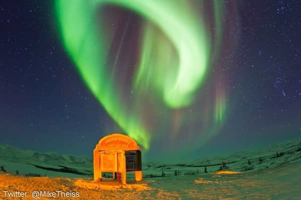 The northern lights above a sign marking the edge of the Arctic Circle.