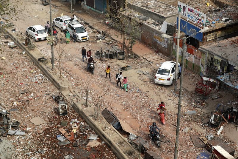 People walk on a road covered with pieces of bricks in a riot affected area following clashes between people demonstrating for and against a new citizenship law in New Delhi