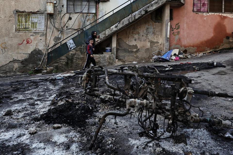 Palestinians walk past a burnt motorcycle following a three-day incursion by the Israeli army on the Jenin camp in the occupied West Bank (AFP via Getty)