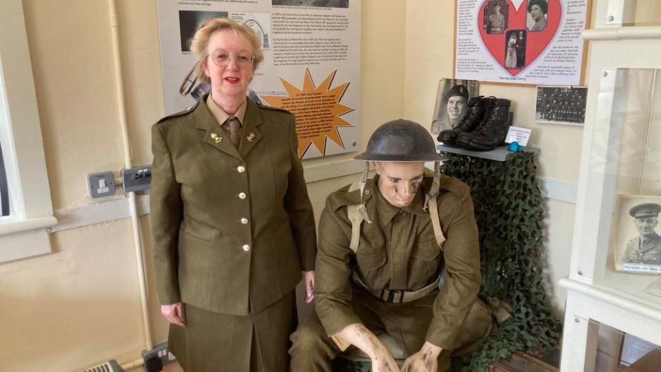 Woman in green army uniform alongside a mannequin in an army uniform