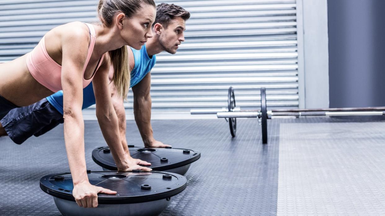  Man and women performing push-ups on balance trainers side by side. 