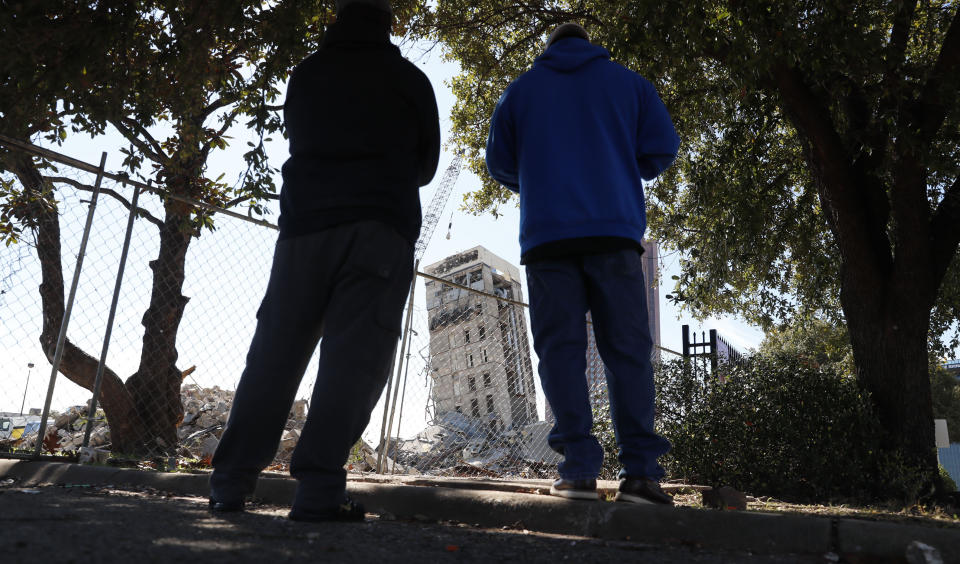 People gather to watch the demolition of the so called "Leaning Tower of Dallas" as a wrecking ball works to topple the structure north of downtown Dallas, Monday, Feb. 24, 2020. The still standing structure is part of an 11-story building that found a second life online after surviving a first demolition attempt. The former Affiliated Computer Services building inspired jokes and comparisons to Italy's Leaning Tower of Pisa when a Feb. 16 implosion failed to bring down its core. The company that engineered the blast said some explosives did not go off. (AP Photo/LM Otero)