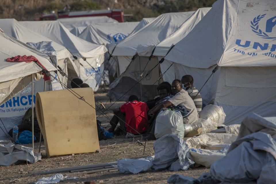 Migrants sit next to the tents at a temporary camp near Mytilene town, on the northeastern island of Lesbos, Greece, Saturday, Sept. 12, 2020. Greek authorities have been scrambling to find a way to house more than 12,000 people left in need of emergency shelter on the island after the fires deliberately set on Tuesday and Wednesday night gutted the Moria refugee camp. (AP Photo/Petros Giannakouris)