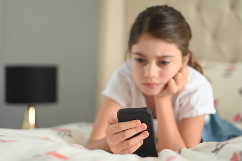 Young girl looks at social media on phone. Her expression is sad or concerned.