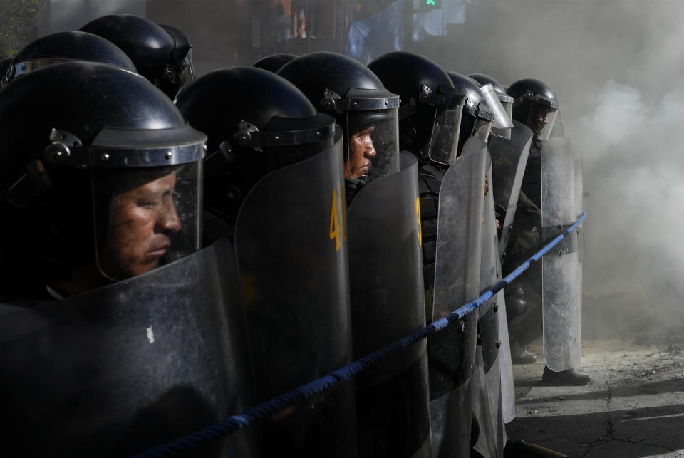 Agentes de policía avanzan en fila hacia una manifestación de maestros en medio de una nube de humo de los extintores y los fuegos artificiales utilizados por los inconformes que protestan contra la jubilación forzosa, en La Paz, Bolivia, el 22 de abril de 2024. (AP Foto/Juan Karita)