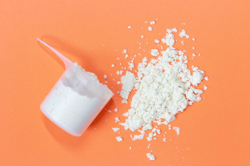 scoop with scattered protein powder, side view on a orange background