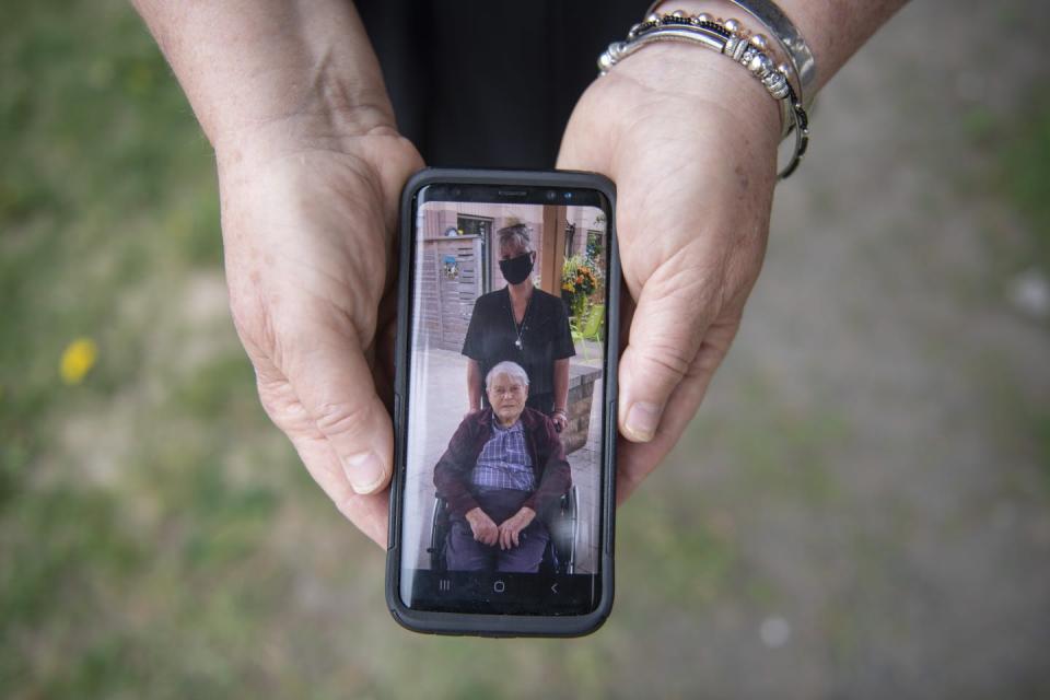 A smartphone in a woman's hands, showing a picture of a woman in a mask and a man in a wheelchair