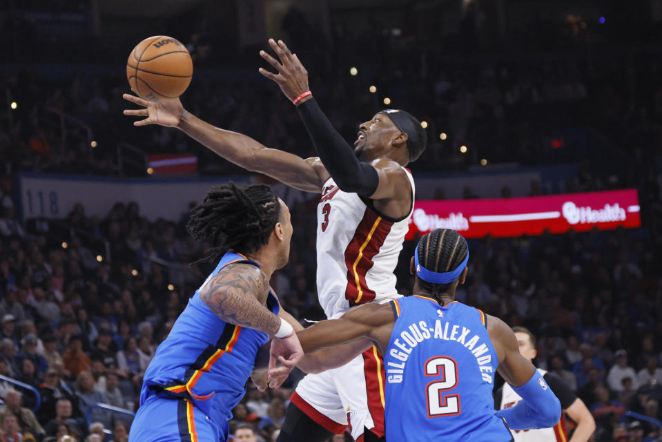 Miami Heat center Bam Adebayo, center, tries to catch the ball near Oklahoma City Thunder forward Jaylin Williams, left, and guard Shai Gilgeous-Alexander (2) during the first half of an NBA basketball game Friday, March 8, 2024, in Oklahoma City. (AP Photo/Nate Billings)