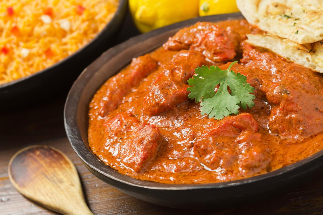 Slow cooker chicken tikka masala in a brown ceramic bowl, selective focus, with naan to the right, next to a wooden spoon, rice in a bowl, and two lemons