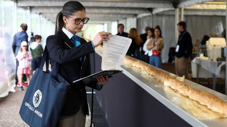 Joanne Brent, adjudicator of the Guinness World Records, stands near the baguette during her inspection during the Suresnes Baguette Show in Suresnes near Paris on May 5. - Stephanie Lecocq/Reuters