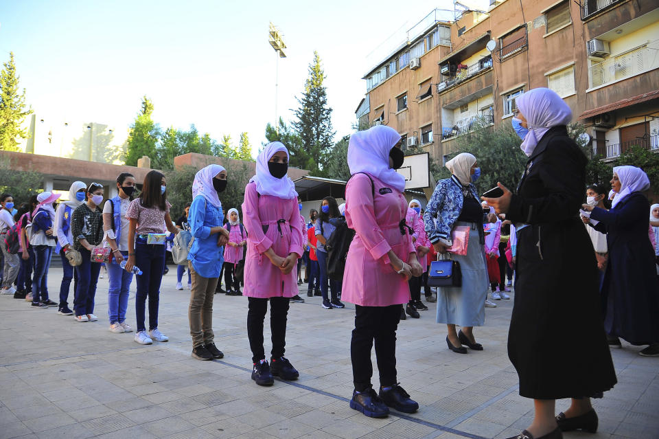 In this photo released by the Syrian official news agency SANA, students wear masks as they wait in line on their first day back at school, in Damascus, Syria, Sunday, Sept. 13, 2020. More than 3 million students went to school in government-held areas around Syria Sunday marking the first school day amid strict measures to prevent the spread of coronavirus. (SANA via AP)