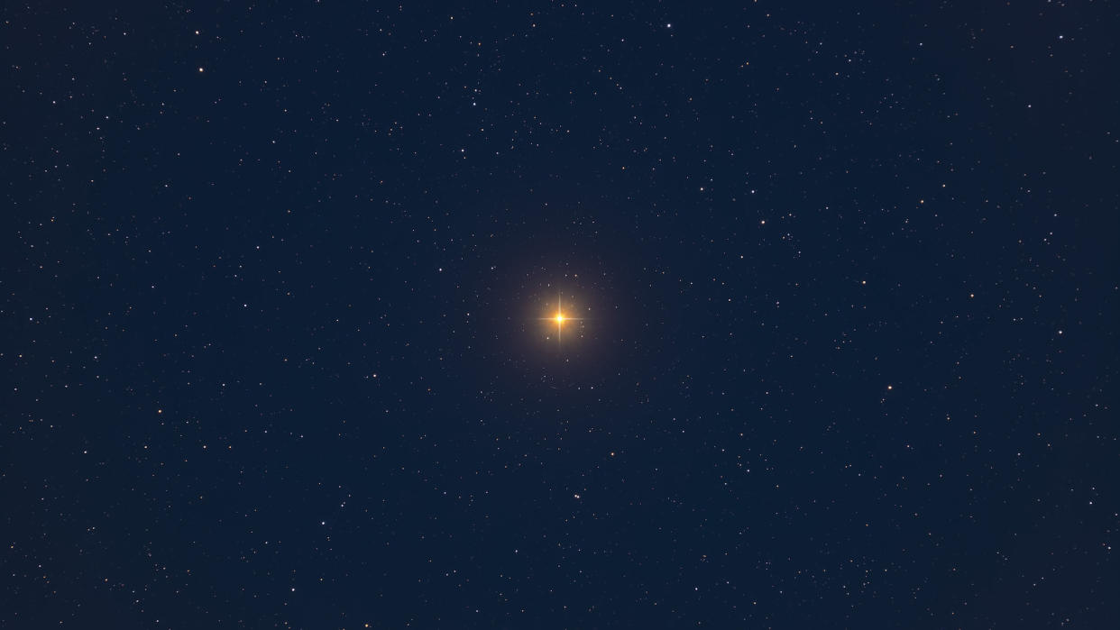  A bright yellow star, shining rays spiked on its sides to from a small "+", hangs in the center of a rich, dark blue, almost black sky. Fainter stars are sprinkled throughout. 
